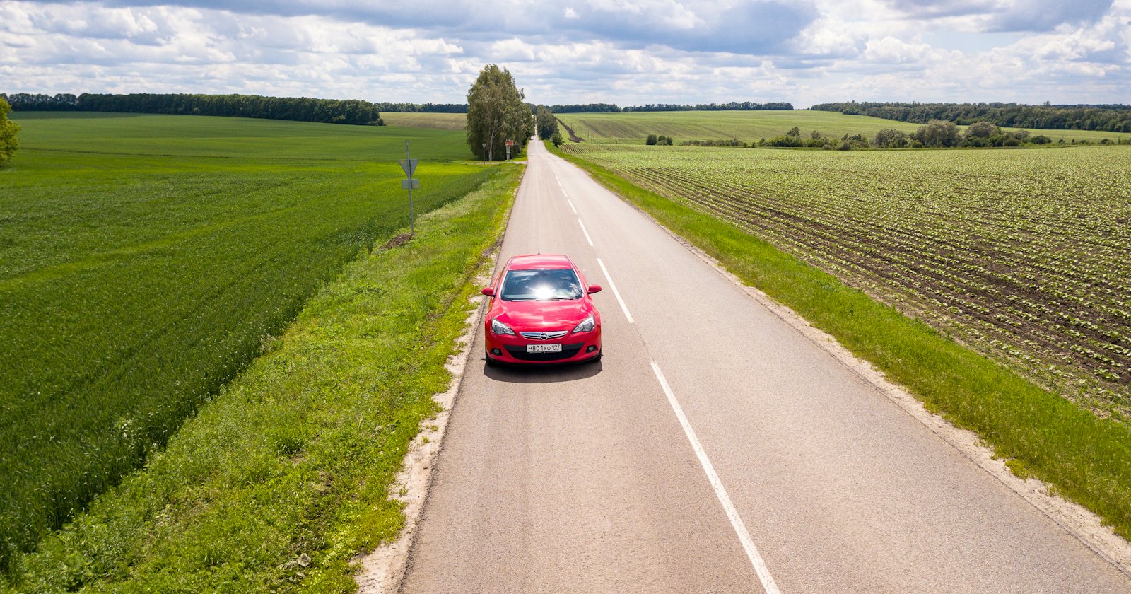 Rotes Auto fährt auf sonniger Straße zwischen grünen Wiesen