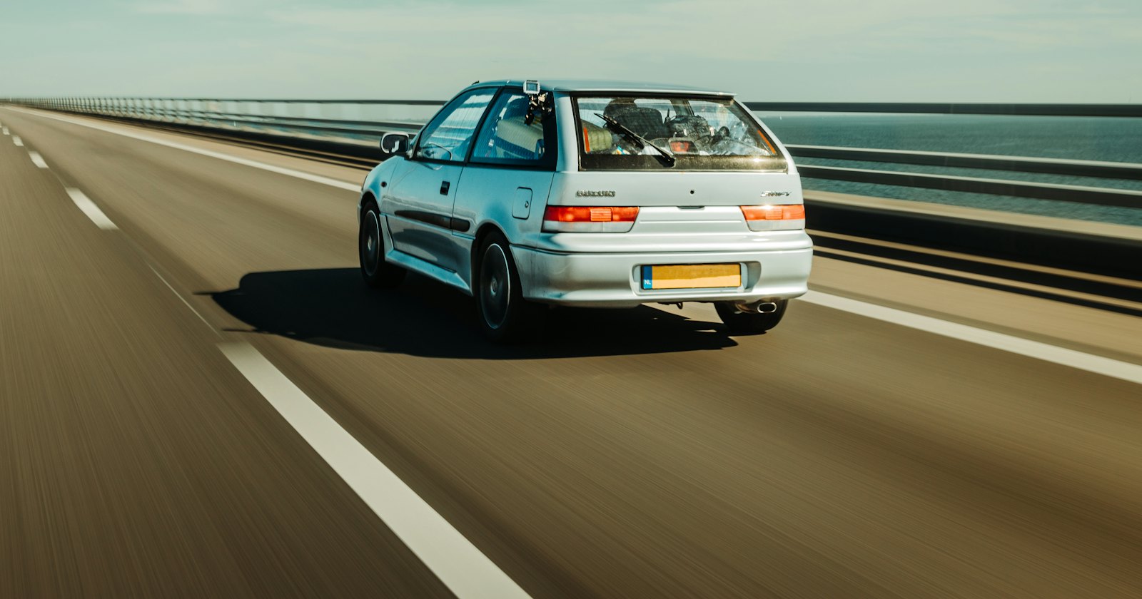 Witte auto rijdend op snelweg langs oceaan in helder daglicht